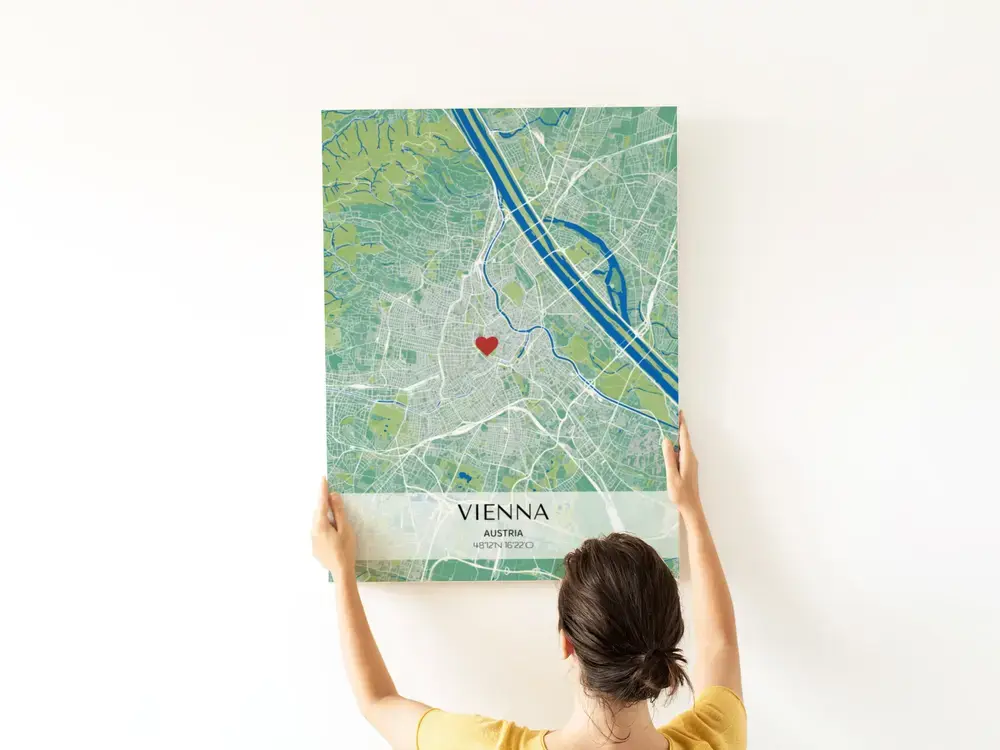 Green and blue city map poster with a heart marker and coordinates on a light banner, displayed on a white wall