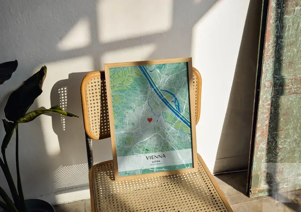 Green and blue city map poster with a heart and coordinates, in a natural wood frame on a sunlit cane chair
